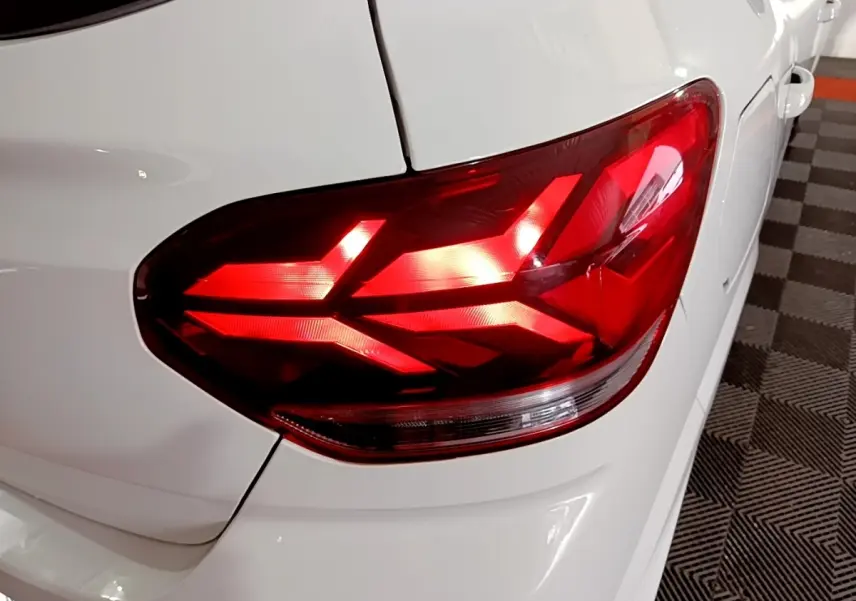 Gros plan sur le feu arrière droit rouge d'une Dacia Sandero blanche, vue partielle du coffre et de la portière arrière.
