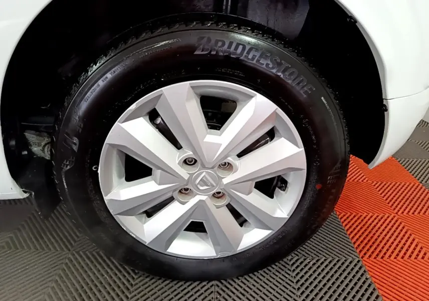 Gros plan sur la roue avant droite d'une Dacia Sandero blanche, pneu Bridgestone visible, sur sol à damiers gris et orange.