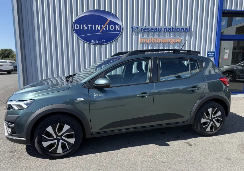 Vue de profil côté gauche d'une Dacia Sandero Stepway 2025 vert cèdre avec jantes distinctives et barres de toit noires.