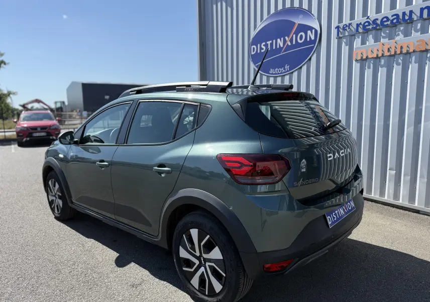 Vue 3/4 arrière droite d'une Dacia Sandero Stepway 2025 vert cèdre avec jantes distinctives et barres de toit noires.