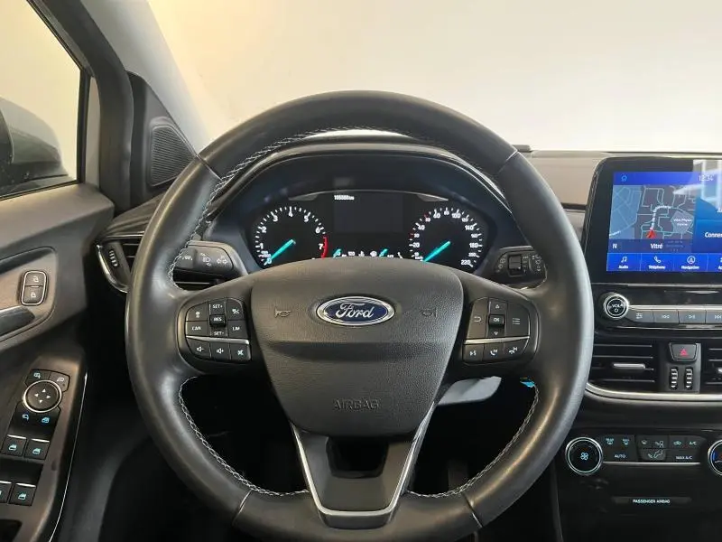 Vue centrée sur le volant cuir multifonction d'une Ford Puma gris Solar avec tableau de bord et écran GPS tactile visible.