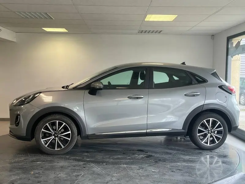 Ford Puma gris Solar métallisée vue de profil côté gauche dans un showroom lumineux avec jantes alu noires et argentées.