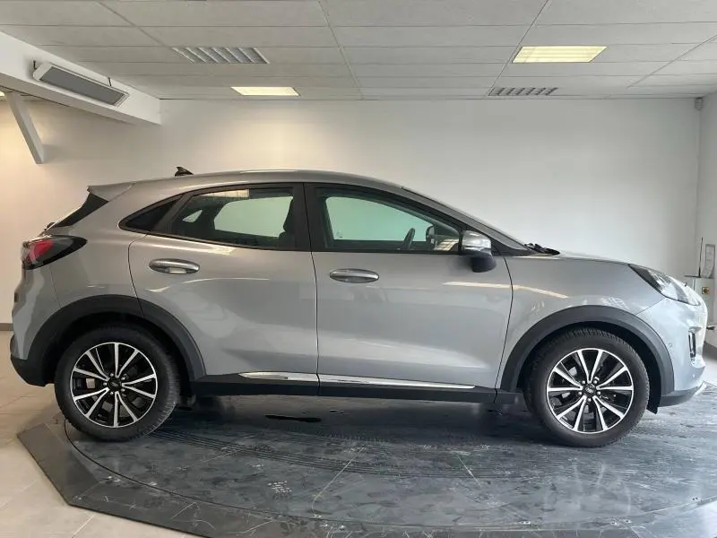 Profil côté droit du Ford Puma gris Solar métallisé 2021, avec jantes alliage et lignes fluides visibles en intérieur showroom.