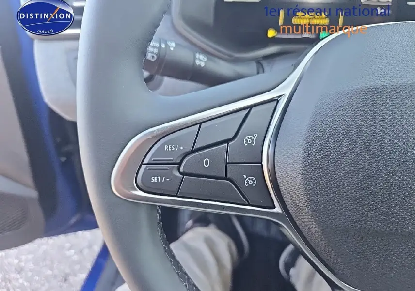Gros plan sur les commandes au volant côté gauche d'une Renault Clio V bleu iron 2025 hybride essence.
