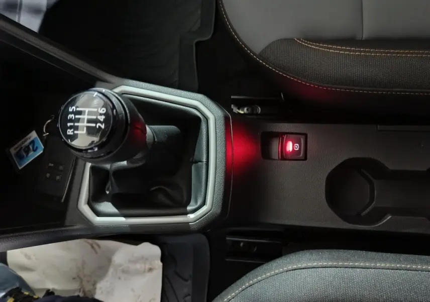 Vue rapprochée de la console centrale de la Dacia Sandero Extreme+ TCe 110 2024, avec levier de vitesse manuel et frein à main électrique allumé.