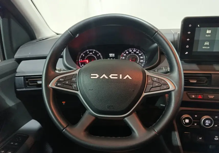 Vue rapprochée du volant cuir multifonctions noir du Dacia Sandero 2024 avec tableau de bord et écran tactile.