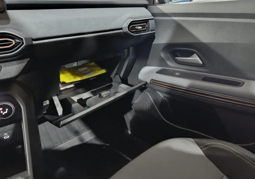 Intérieur de la Dacia Sandero Extreme+ 2024, vue côté passager sur la boîte à gants ouverte et la porte avec insert décoratif.