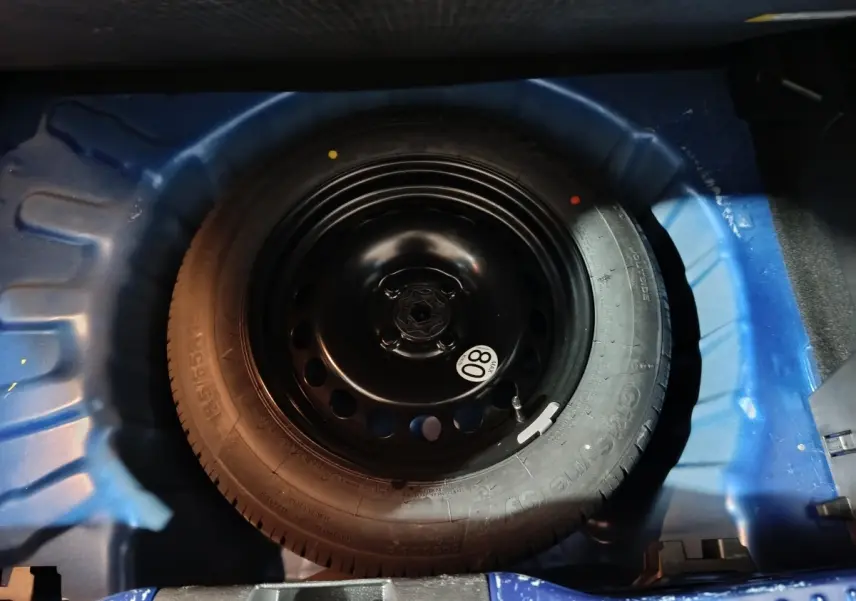 Roue de secours galette en jante acier noir dans le coffre bleu d'une Dacia Sandero Extreme+ TCe 110 2024.