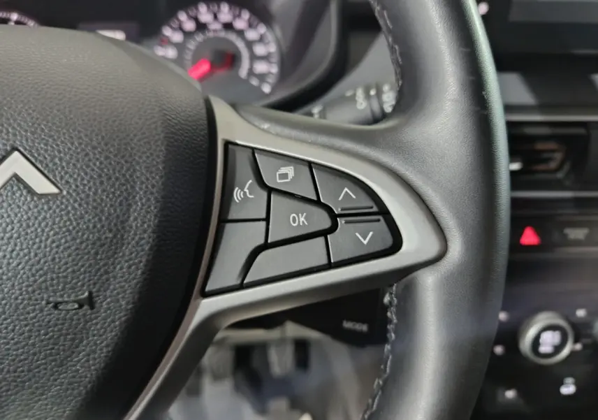 Gros plan sur le volant cuir noir de la Dacia Sandero 2024 avec commandes multifonctions et tableau de bord flou.