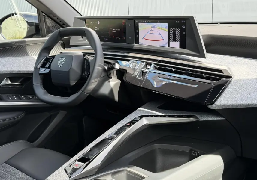 Vue intérieure côté conducteur du Peugeot 3008 Hybrid 2025, volant compact et double écran HD affichant caméra de recul.