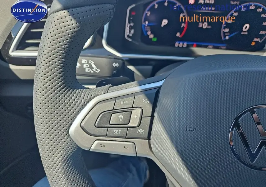 Gros plan sur le volant cuir perforé côté gauche du Volkswagen T-Roc noir perle avec commandes multifonctions et tableau de bord numérique.