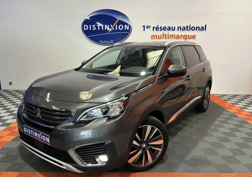 Vue 3/4 avant d'un Peugeot 5008 gris métallisé, avec jantes alliage et feux allumés en showroom.