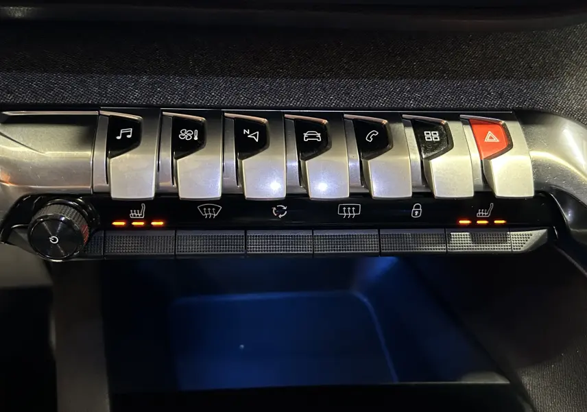 Gros plan sur la rangée de boutons argentés du tableau de bord du Peugeot 5008 gris, avec sièges chauffants activés.