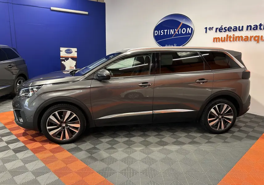 Peugeot 5008 gris métallisé vue de profil côté gauche, avec jantes alliage et vitres teintées dans un showroom.