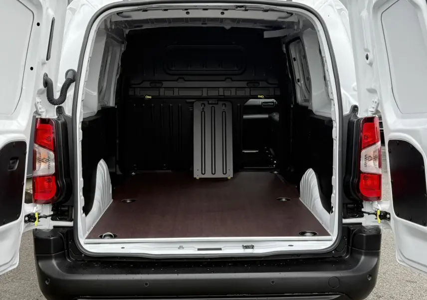 Vue arrière ouverte du Peugeot Partner blanc 2025, montrant l'espace de chargement avec plancher bois antidérapant et anneaux d'arrimage.