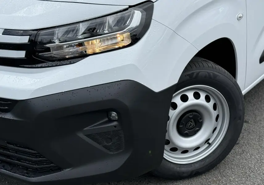 Gros plan sur l'avant droit blanc du Peugeot Partner XL 2025, mettant en valeur le phare allumé et la roue acier.