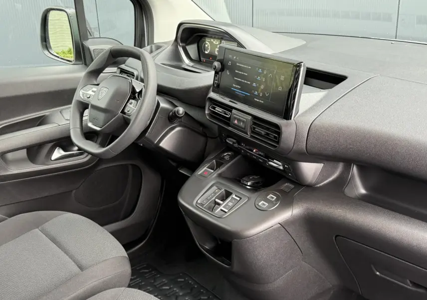 Vue intérieure côté conducteur du Peugeot Partner 2025, tableau de bord noir avec écran tactile et volant multifonctions.