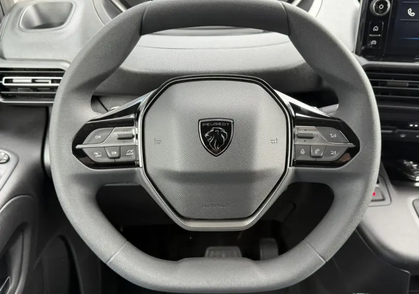 Vue rapprochée du volant multifonctions noir du Peugeot Partner 2025 avec logo lion au centre et commandes intégrées.