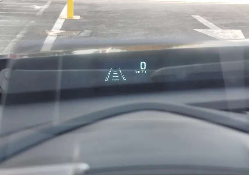 Affichage tête haute du Mazda CX-3 bleu Dynamic Mica montrant la vitesse à 0 km/h et l'alerte de maintien de voie.