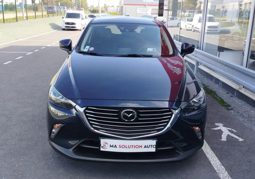 Vue frontale d'un Mazda CX-3 2016 bleu Dynamic Blue Mica avec calandre chromée et phares LED allumés.