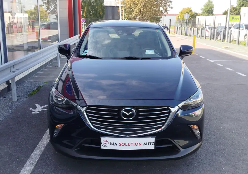 Vue frontale d'un Mazda CX-3 2016 bleu foncé avec calandre chromée et phares LED allumés.