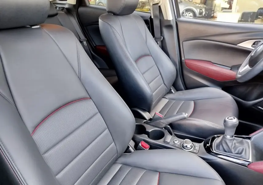 Vue intérieure côté conducteur du Mazda CX-3 2016, sièges cuir noir avec surpiqûres rouges et détails rouges sur les portes.