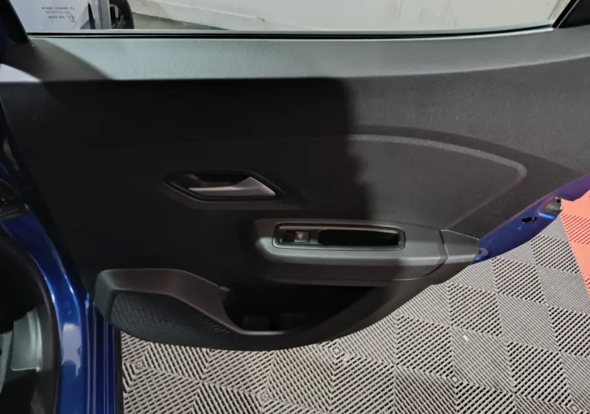 Vue intérieure de la porte côté gauche d’une Dacia Sandero Extreme+ TCe 110 bleu, avec poignée et commande de lève-vitre.