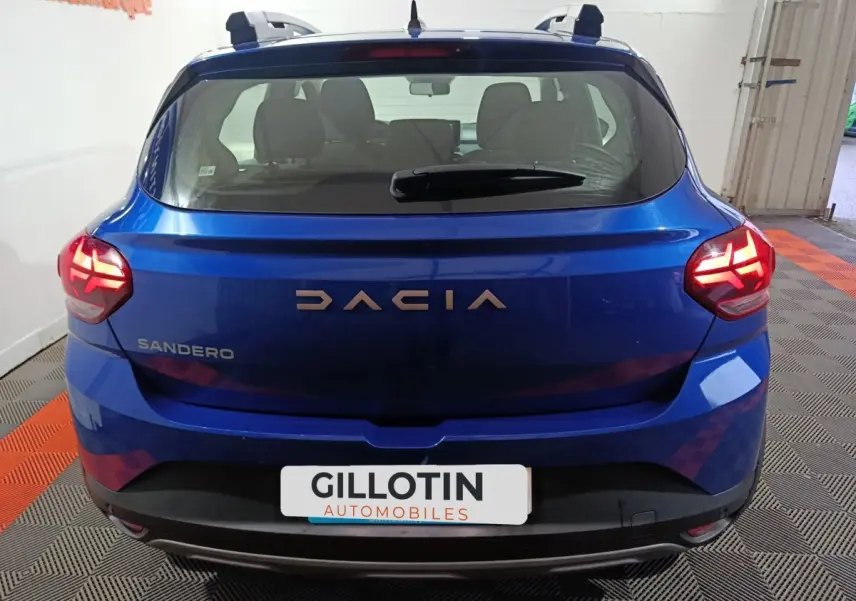 Vue arrière d'une Dacia Sandero Extreme+ TCe 110 bleu 2024 avec feux LED allumés et toit équipé de rails assortis.