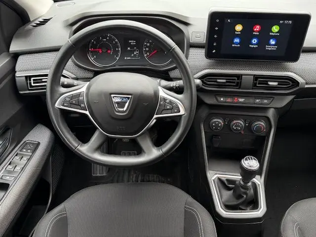 Vue intérieure centrée sur le volant et la console centrale d'une Dacia Sandero blanche glacier, avec écran tactile et boîte manuelle.