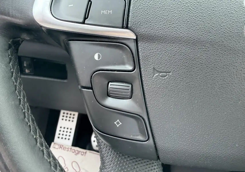 Gros plan sur les commandes noires au volant cuir du Citroën DS4, avec pédales sport en aluminium en arrière-plan.