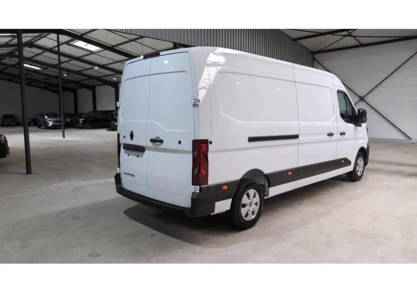 Renault Master blanc vu en 3/4 arrière droit dans un grand garage, avec feux arrière verticaux et protections noires.