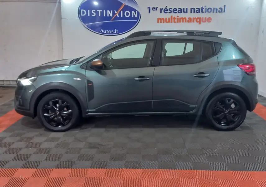 Vue de profil côté gauche d'une Dacia Sandero Extreme+ TCe 110 2024 vert foncé avec jantes noires et barres de toit.