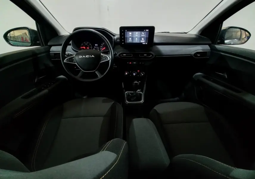 Vue intérieure avant de la Dacia Sandero 2024, tableau de bord avec écran tactile central et volant multifonctions noir.