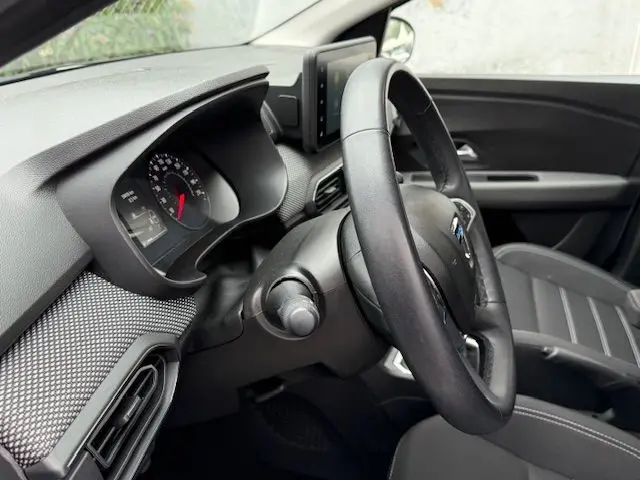 Vue intérieure côté conducteur du Dacia Sandero blanc glacier 2023, avec tableau de bord et volant en cuir noir.
