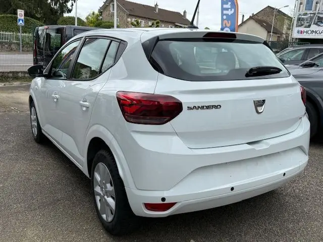 Vue 3/4 arrière droite d'une Dacia Sandero blanche Glacier 2023, avec feux arrière rouges et logo distinctif sur le hayon.