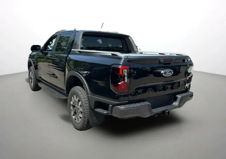 Ford Ranger 2025 noir agate vu en 3/4 arrière droit, avec benne fermée et jantes tout-terrain Wildtrak Plus.