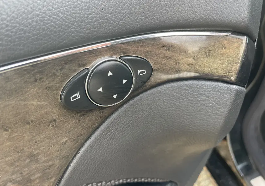 Détail du panneau de commande des rétroviseurs sur la portière côté gauche d'une Mercedes Classe E noire de 2003.