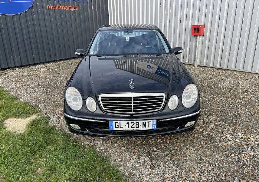 Vue avant d'une Mercedes Classe E 320 CDI noire de 2003, avec calandre chromée et phares ronds doubles visibles.