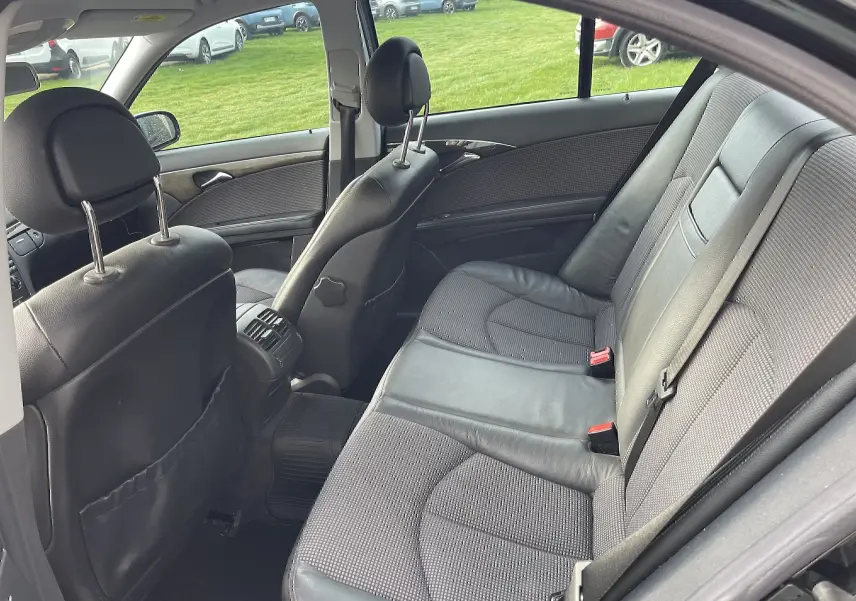 Vue intérieure côté droit montrant la banquette arrière en cuir et tissu gris d'une Mercedes Classe E noire de 2003.