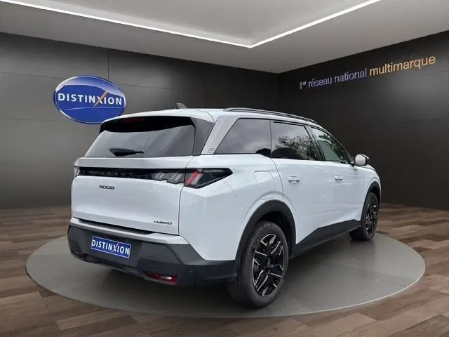 Vue 3/4 arrière droite du Peugeot 5008 blanc hybride 2025 avec jantes noires et feux arrière LED distinctifs.