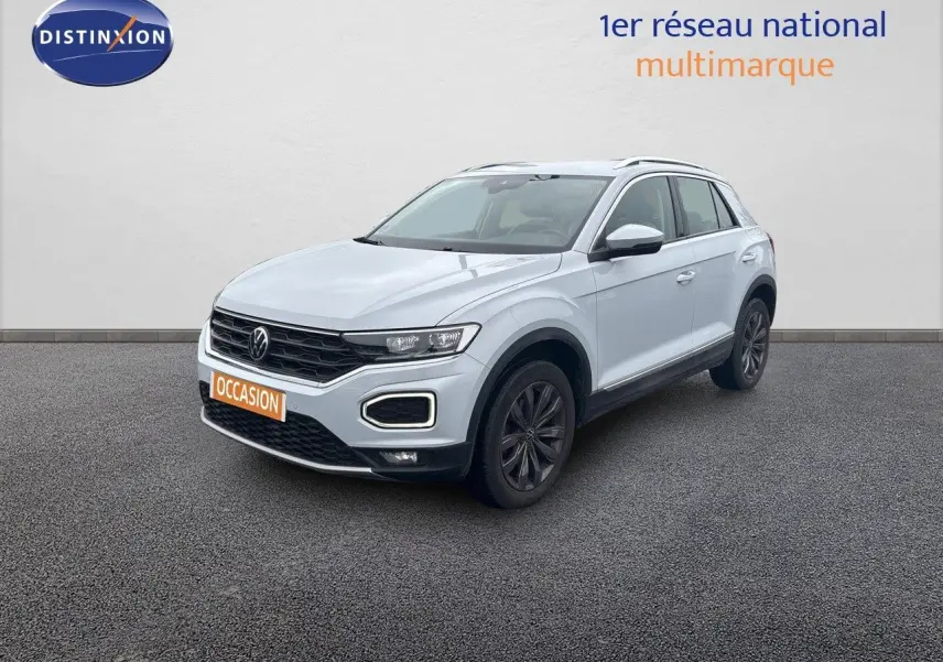 Volkswagen T-Roc blanc argenté en 3/4 avant droit, avec calandre noire et jantes foncées sur sol gris.