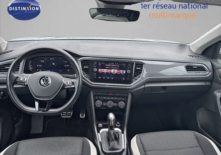 Vue intérieure avant du Volkswagen T-Roc 1.5 TSI 150 CH Carat avec tableau de bord moderne et sièges tissu noir et blanc.