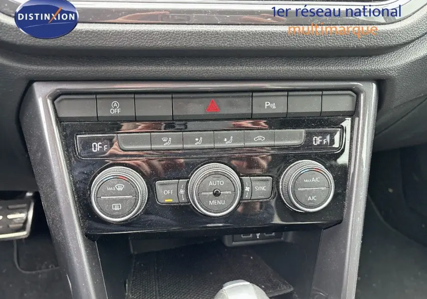 Gros plan sur la console centrale du Volkswagen T-Roc blanc, montrant les commandes de climatisation automatique et boutons de sécurité.
