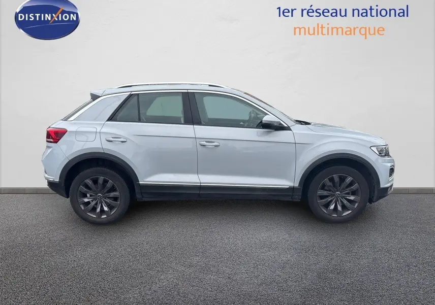 Profil côté gauche d'un Volkswagen T-Roc blanc argenté 2021 avec jantes foncées sur fond neutre.