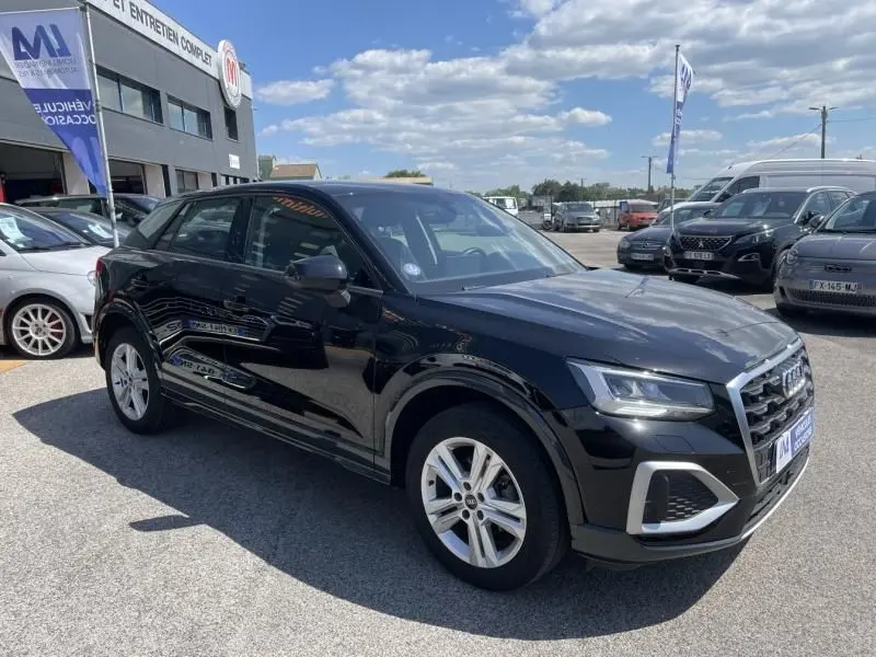 Audi Q2 noir métal en 3/4 avant droit, avec calandre distinctive et jantes alliage visibles, stationné en extérieur.