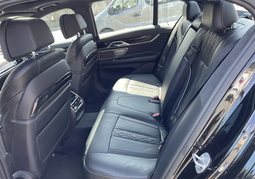 Vue intérieur arrière côté droit d'une BMW Série 7 noire avec sièges en cuir noir matelassé et finitions élégantes.