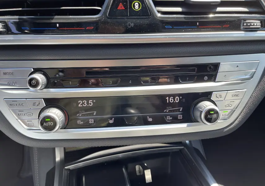 Vue rapprochée de la console centrale de la BMW Série 7 noire, montrant les commandes de climatisation digitale et boutons multifonctions.