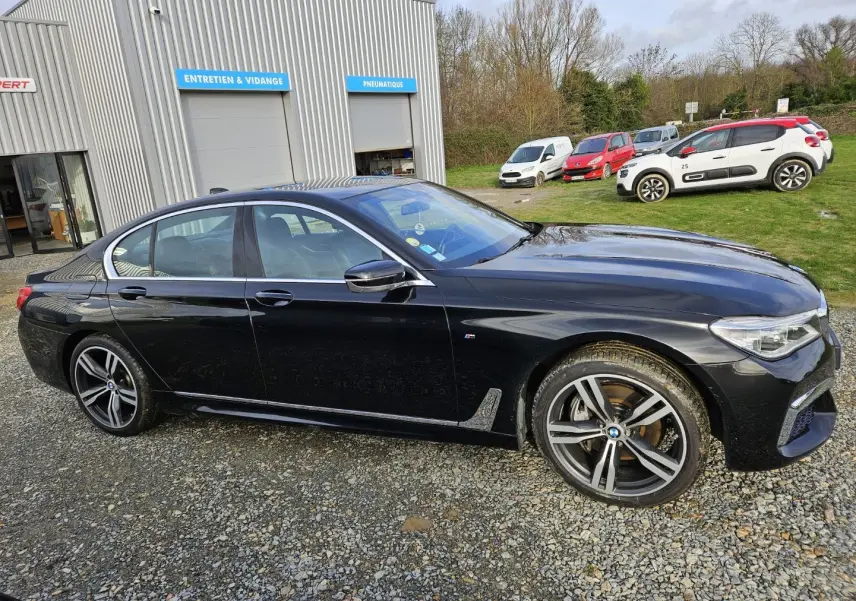 BMW Série 7 G11 noire vue de profil côté gauche, avec jantes sport et détails M Sport visibles.