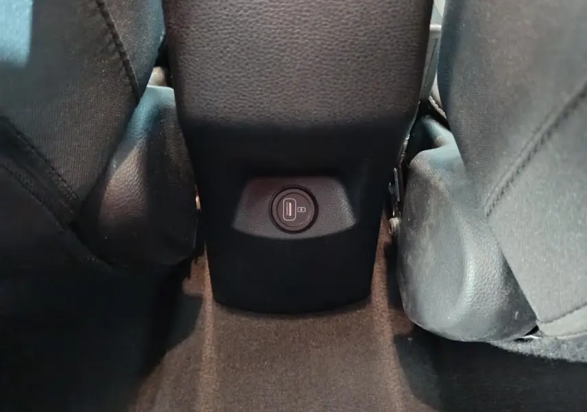 Prise USB arrière entre les sièges noirs du Kia Stonic 1.0 T-GDI 100 Urban gris clair, vue rapprochée du plancher.