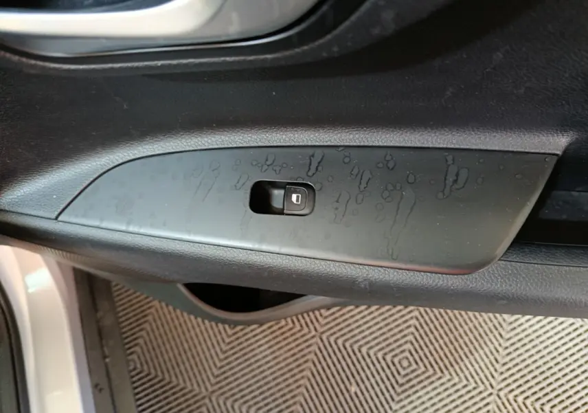 Gros plan sur le bouton de verrouillage des portes côté conducteur d’un KIA Stonic gris clair, intérieur noir.